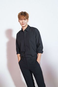 a young man standing in front of a white wall wearing black pants and a black shirt