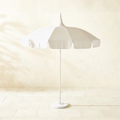 an umbrella on a white stand in front of a beige wall with shadow from the sun