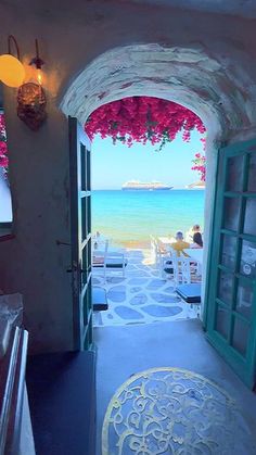 an open door leading to the beach with flowers hanging from it's sides and people sitting at tables on either side