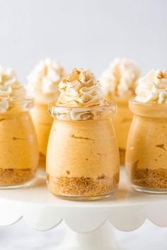 small jars filled with desserts on top of a white cake platter and topped with whipped cream