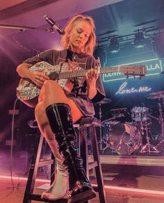 a woman sitting on top of a stool holding a guitar in front of a microphone