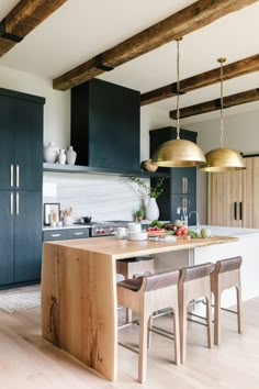 a kitchen with black cabinets and gold pendant lights hanging from the ceiling over an island