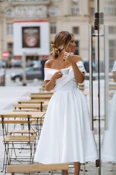 a woman in a white dress standing next to a table with chairs and tables behind her