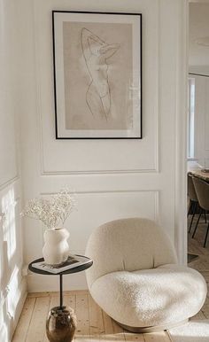 a room with a chair, table and vase on the floor in front of a painting