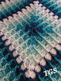 a crocheted blanket is shown with the words tgs written in white and blue