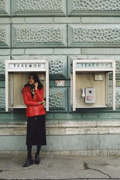 a woman in red jacket standing next to two mailboxes on the side of a building