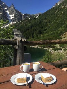 two cups of coffee and cake on a table with mountains in the background