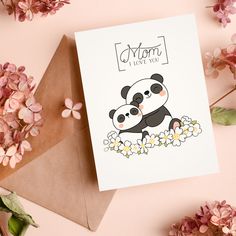 a card with a panda bear holding flowers on top of an envelope next to some pink flowers