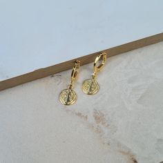 two pairs of gold earrings on a white surface