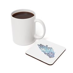 a cup of coffee sitting next to a white mug on a coaster with a blue tiger design