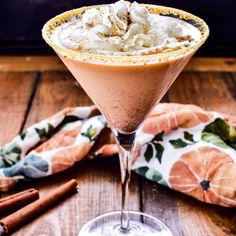 a drink in a martini glass garnished with whipped cream and cinnamon sticks on a wooden table