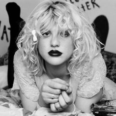 a woman laying on top of a bed with her hands under her chin and black lips