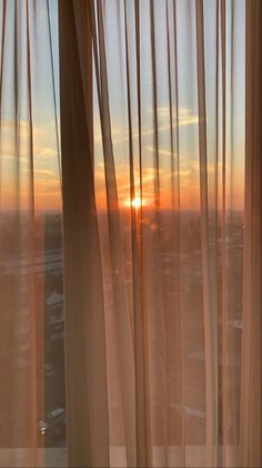 the sun is setting behind sheer curtains