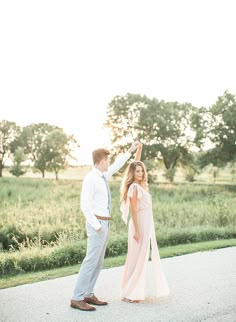 a man and woman dancing in the middle of an open road with trees in the background