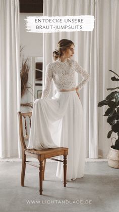 a woman standing in front of a window wearing a long sleeved wedding dress with an open back