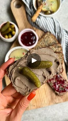 a person holding a piece of bread with pickles on it in front of other foods