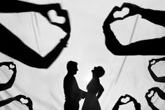 the silhouettes of two people holding hands in front of a white background with heart shapes