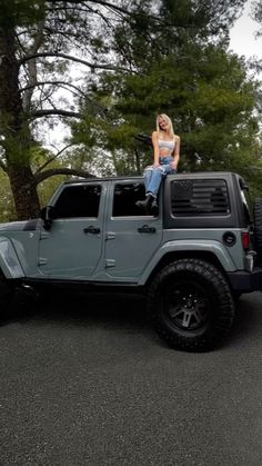 a woman sitting on top of a gray jeep