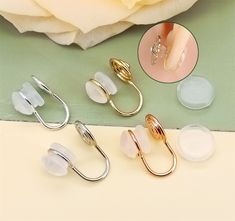 three pairs of metal clips with white and gold rings on them next to a rose