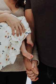 a man and woman holding the hand of a baby in their arms while standing next to each other