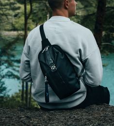 a man with a backpack sitting on a rock looking out at the water and trees