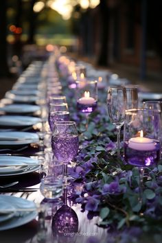 a long table is set with purple flowers and candles for an elegant dinner or party