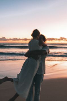 a man and woman hugging on the beach at sunset