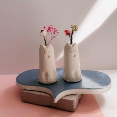 two small white vases with flowers in them sitting on a blue and pink plate