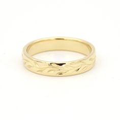 a gold wedding ring with leaves on it, sitting on top of a white surface