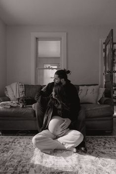 a man and woman sitting on the floor in front of a couch with their arms around each other