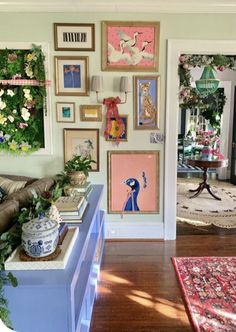 a living room filled with lots of pictures and plants on the wall next to a couch