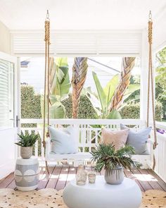 a porch swing with pillows and plants on it