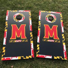 two cornhole game boards with the letters m and m on them sitting in grass