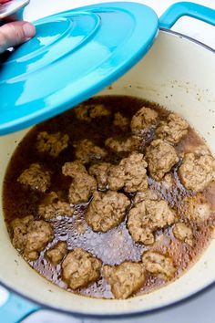 a blue pot filled with meatballs on top of a stove next to a person's hand