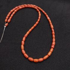 an orange beaded necklace on a black surface with a metal hook in the middle