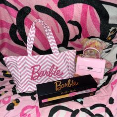 a pink and white bag sitting on top of a bed next to some makeup products