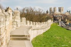 a stone wall with steps leading up to it and the city in the background on a sunny day