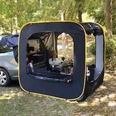 a car is parked next to a tent in the woods with a dog inside it