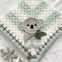 a crocheted blanket with a koala bear on it next to some flowers