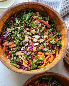 a salad in a wooden bowl on top of a white table next to other dishes