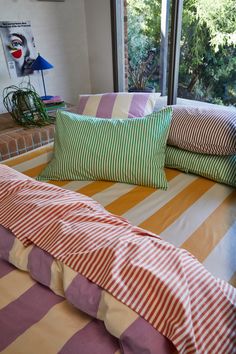 a bed with striped sheets and pillows in front of a large window overlooking the trees