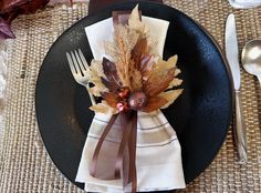 a black plate topped with a fork and napkin covered in fall leaves on top of a table