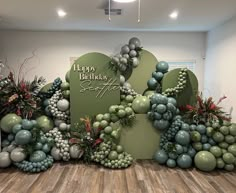 a happy birthday sign surrounded by balloons and greenery in an office setting with wood flooring