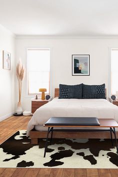 a bed sitting on top of a wooden floor next to two windows in a bedroom