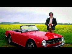 a man standing next to a red sports car in a field with yellow wildflowers