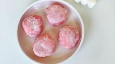 four pink donuts sitting in a white bowl next to some marshmallows