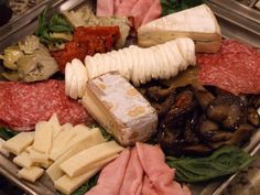 an assortment of meats and cheeses in a metal tray on a counter top