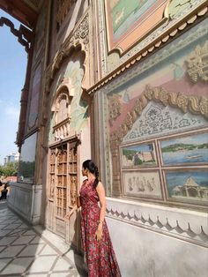 a woman in a red dress leaning against a wall with paintings on the walls behind her