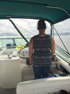 a woman standing on the back of a boat looking out at the water and land