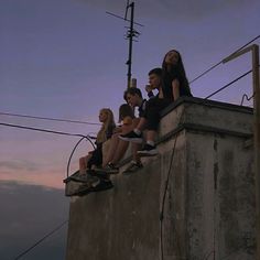 four people sitting on top of a concrete structure with wires above them and one person standing in the distance